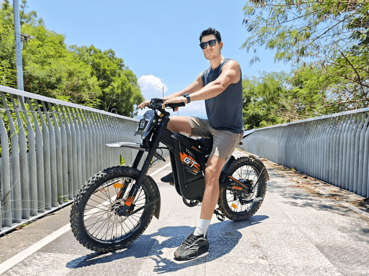 GT2000 elektrinis dviratis 1000W – bekelės elektrinis dviratis su pakelta priekine šake ir grubiu protektoriumi, stovintis ant smėlio.