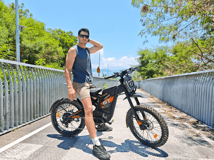 GT2000 elektrinis dviratis 1000W – elektrinis dviratis su vairuotoju, stovintis ant pėsčiųjų tilto, matomos plačios padangos ir diskiniai stabdžiai.