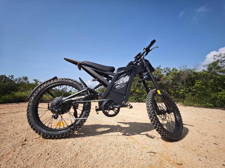 GT2000 elektrinis dviratis 1000W – juodos spalvos elektrinis dviratis su storomis bekelės padangomis, pastatytas ant žvyruoto kelio gamtos apsuptyje.