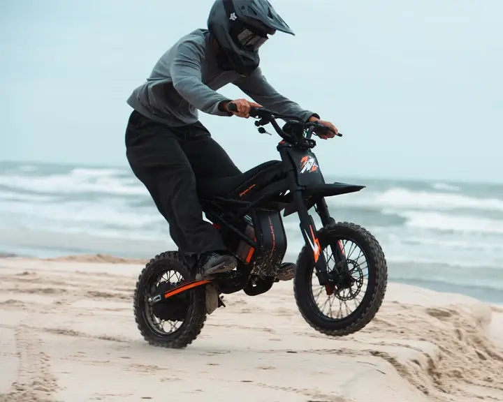 GT54 PRO elektrinis motociklas 1500W važiuoja smėliu paplūdimyje, motociklininkas su šalmu demonstruoja bekelės galią ir stabilumą prie jūros krantinės
