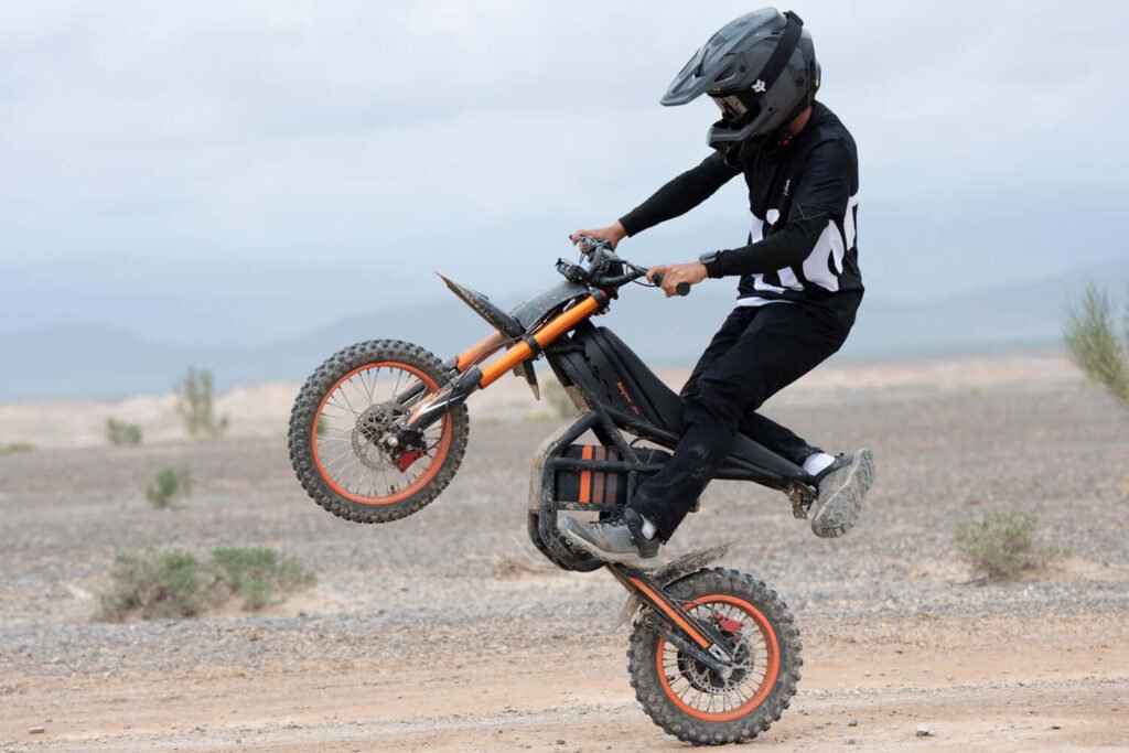 GT54 elektrinis motociklas 1000W – vairuotojas važiuoja per smėlį ir daro „wheelie“ manevrą
