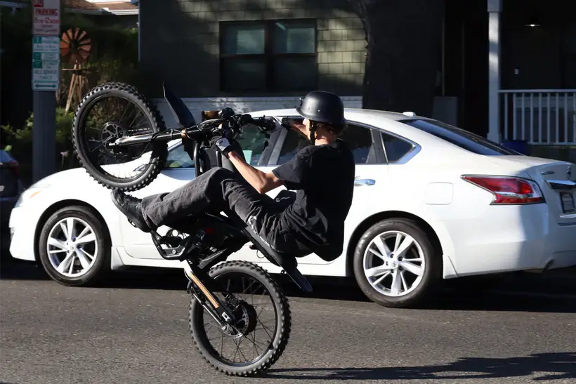 GT73 PRO elektrinis dviratis 1500W atliekantis wheelie miesto gatvėje su motociklininku