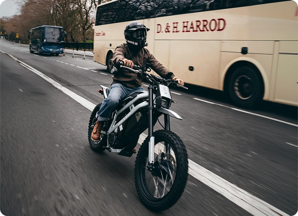 EM23 elektrinis motociklas 2500W važiuoja miesto keliu šalia autobuso.
